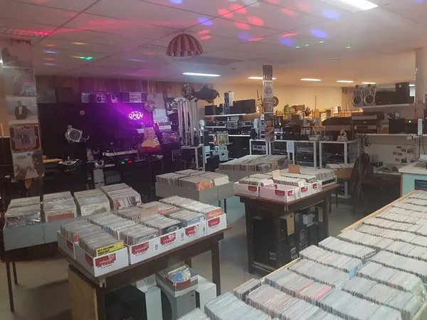 Winkelvloer met tafels vol CDs en vinyl records, stellingen met muziekuitrusting en neonverlichting op de achtergrond