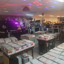 Winkelvloer met tafels vol CDs en vinyl records, stellingen met muziekuitrusting en neonverlichting op de achtergrond