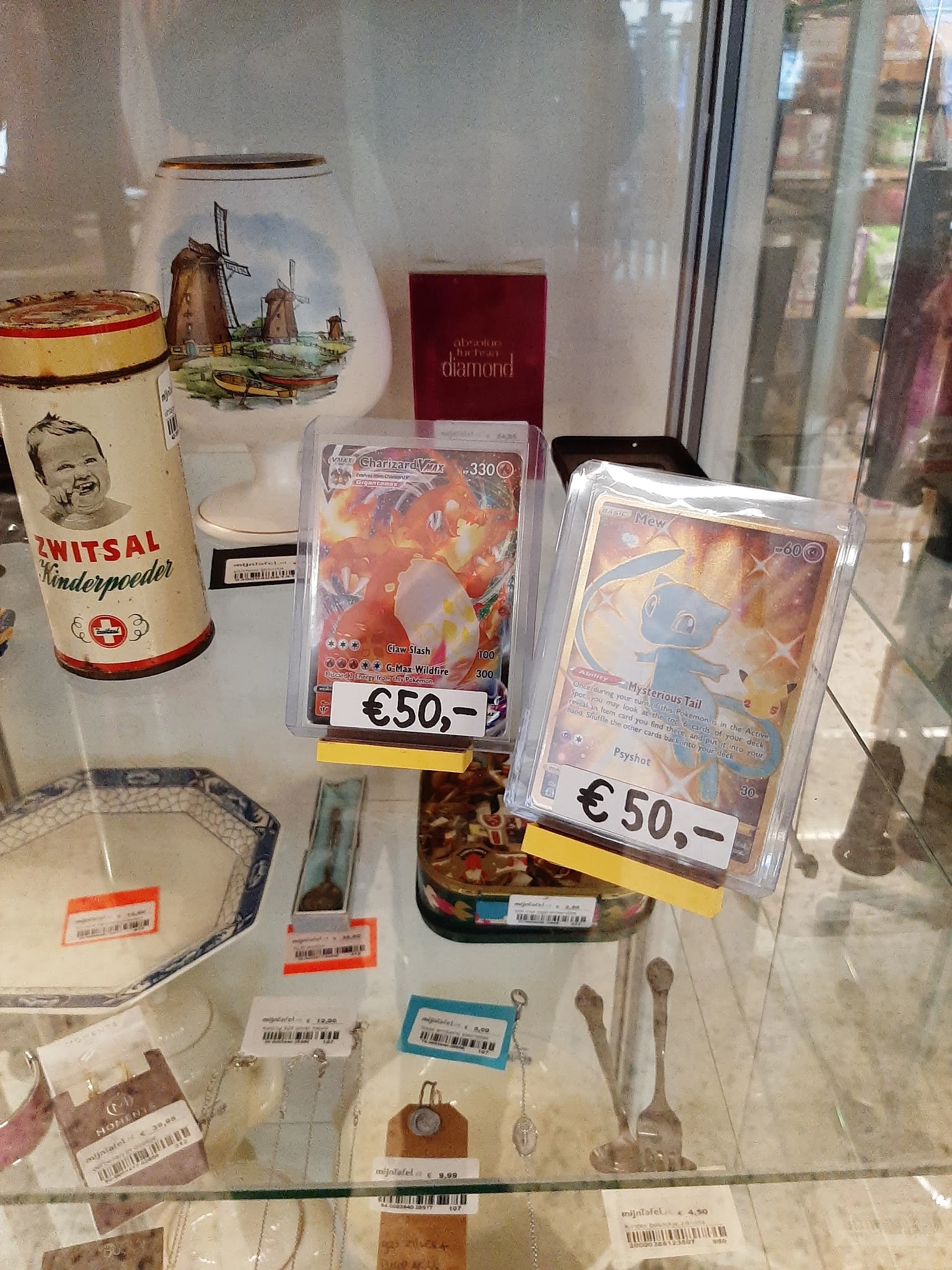 Vitrinekast met verzamelobjecten: vintage blikken, Pokemon-kaarten en andere collectibles met prijskaartjes.