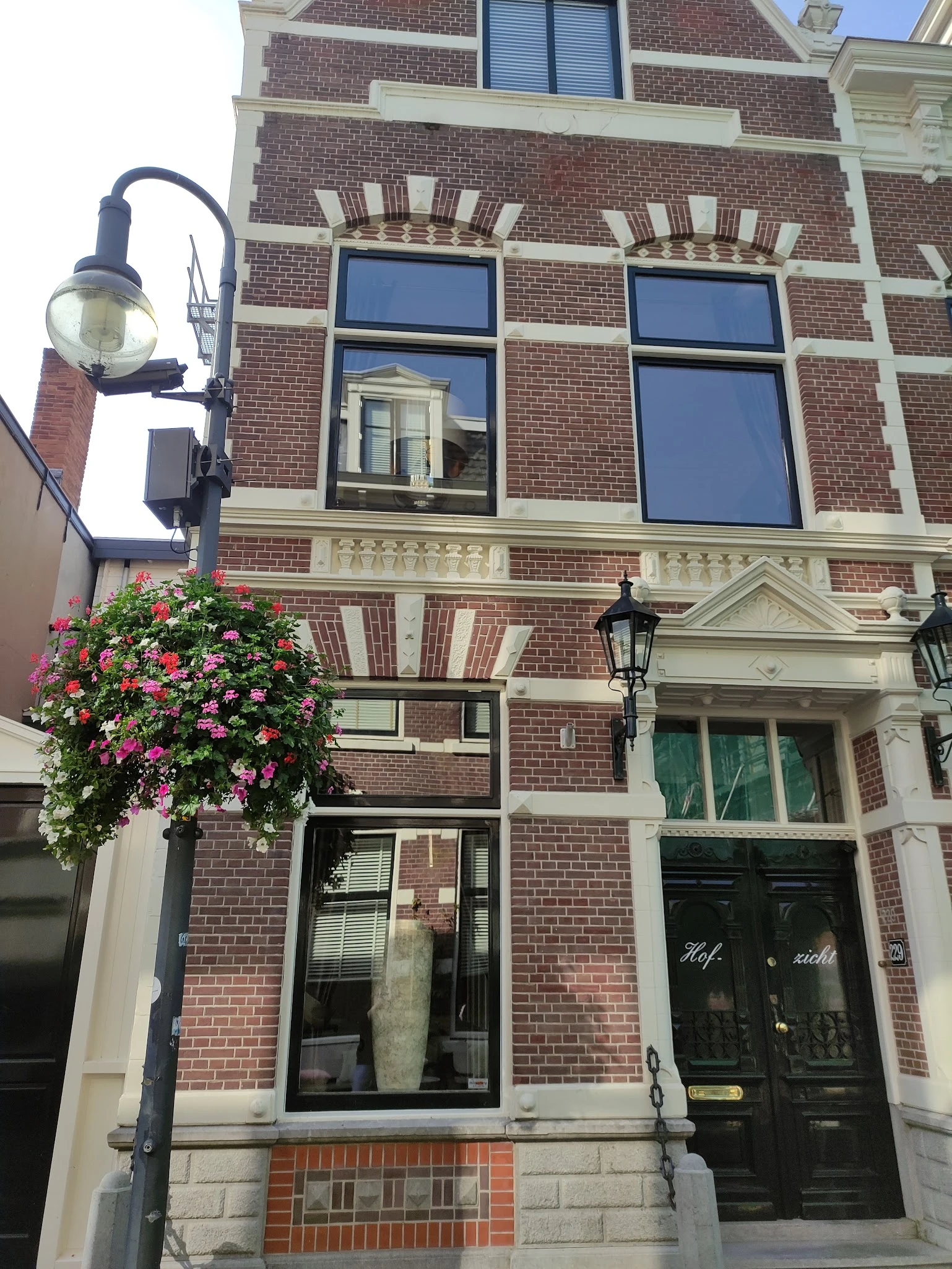Bakstenen gevel van een historic pand met groene deuren en een bloeiende bloembak aan de straatkant