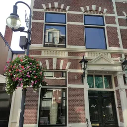 Bakstenen gevel van een historic pand met groene deuren en een bloeiende bloembak aan de straatkant