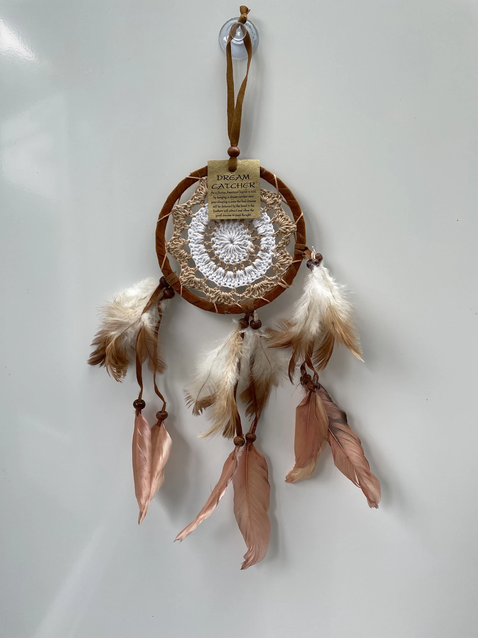 Bruine dreamcatcher met witte veren en roze linten tegen een witte muur