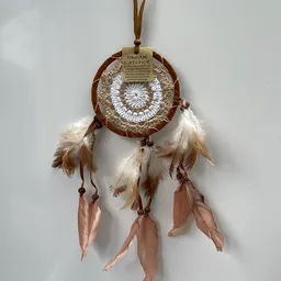 Bruine dreamcatcher met witte veren en roze linten tegen een witte muur