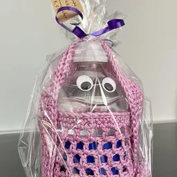 Tweedehands glazen vaas met roze gebreide muts en paarse strik, verpakt in cellofaan