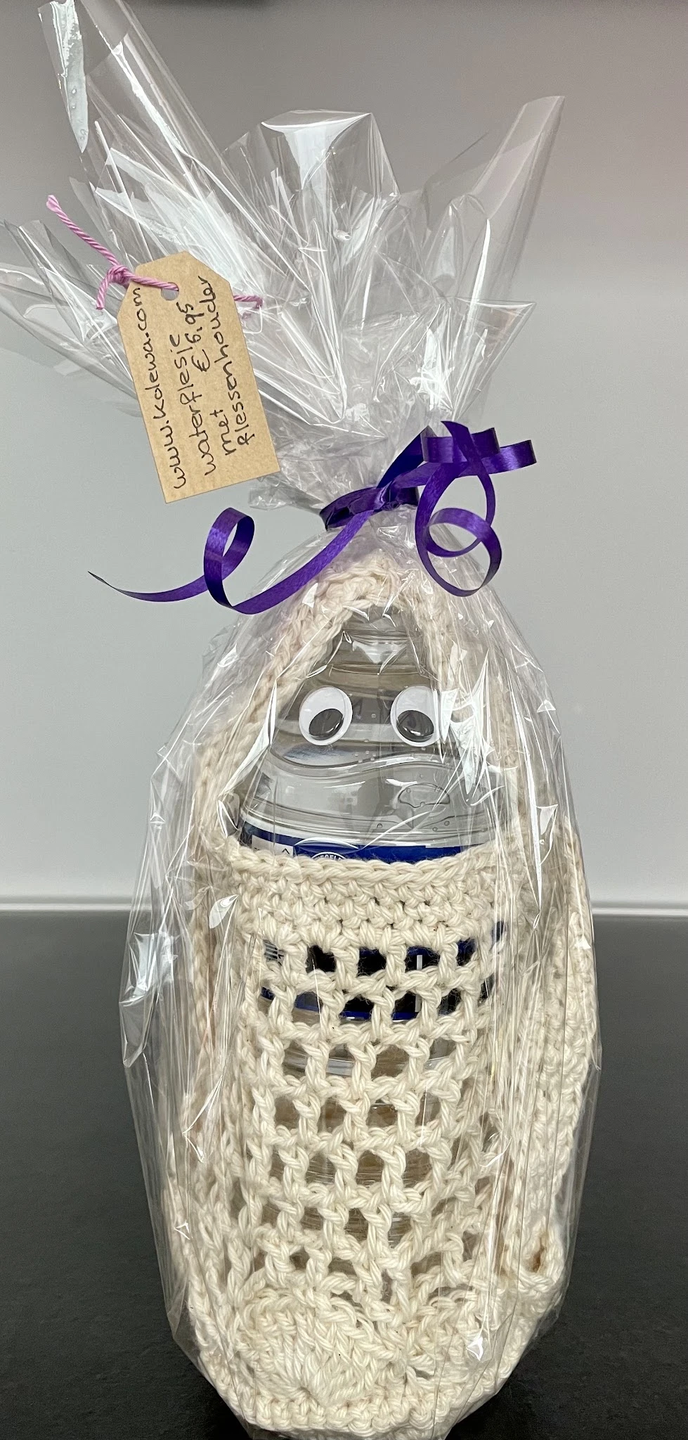 Handgemaakte decoratieve pop met witte kralen lichaam, googly eyes en paarse strik, verpakt in celofaan met paars lint.