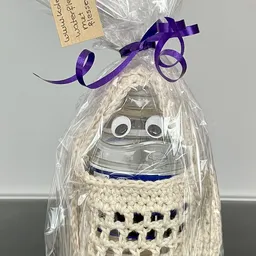 Handgemaakte decoratieve pop met witte kralen lichaam, googly eyes en paarse strik, verpakt in celofaan met paars lint.