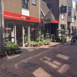 Winkelgevel van mijn Tafel met rode luifel, glazen pui en potplanten op de stoep