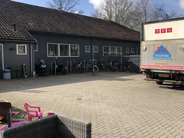 Donkergrijs pand met parkeerplaats vol fietsen en een vrachtwagen ernaast