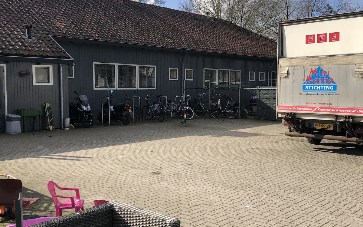 Donkergrijs pand met parkeerplaats vol fietsen en een vrachtwagen ernaast