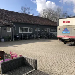 Donkergrijs pand met parkeerplaats vol fietsen en een vrachtwagen ernaast