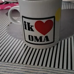 Witte mok met opdruk 'ik hou van OMA' en rood hart op gestreepte ondergrond
