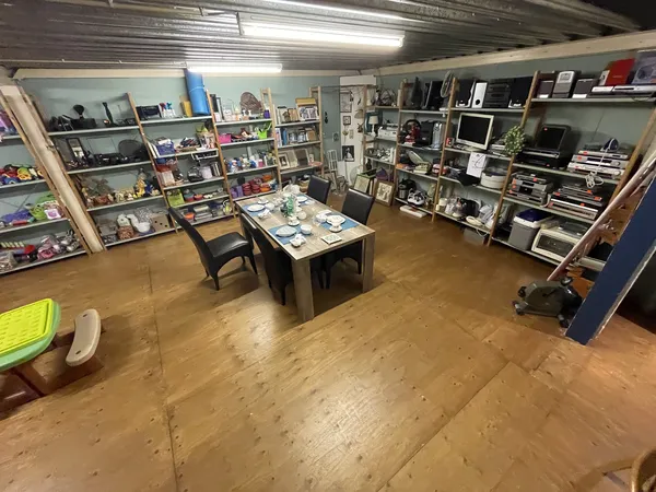 Winkelvloer met houten planken, stellingen met boeken en spullen aan alle zijden, centrale tafel met zwarte stoelen