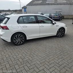 Witte Volkswagen Golf met zwarte velgen op het parkeerterrein tussen andere auto's