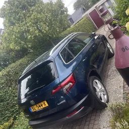 Donkerblauwe Kia-auto van boven gezien op parkeerplaats naast gebouw met klimop