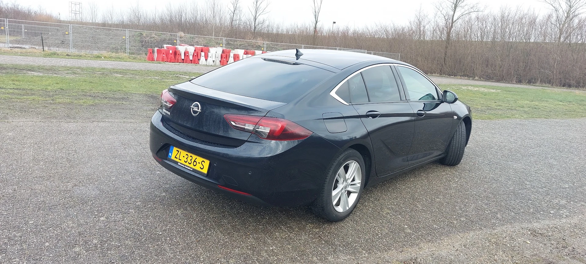 Zwarte Opel sedan geparkeerd op een terrein, gezien van opzij achter