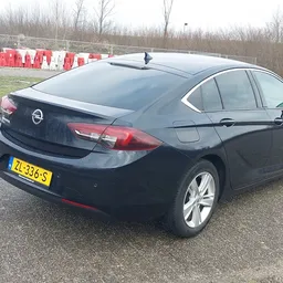 Zwarte Opel sedan geparkeerd op een terrein, gezien van opzij achter