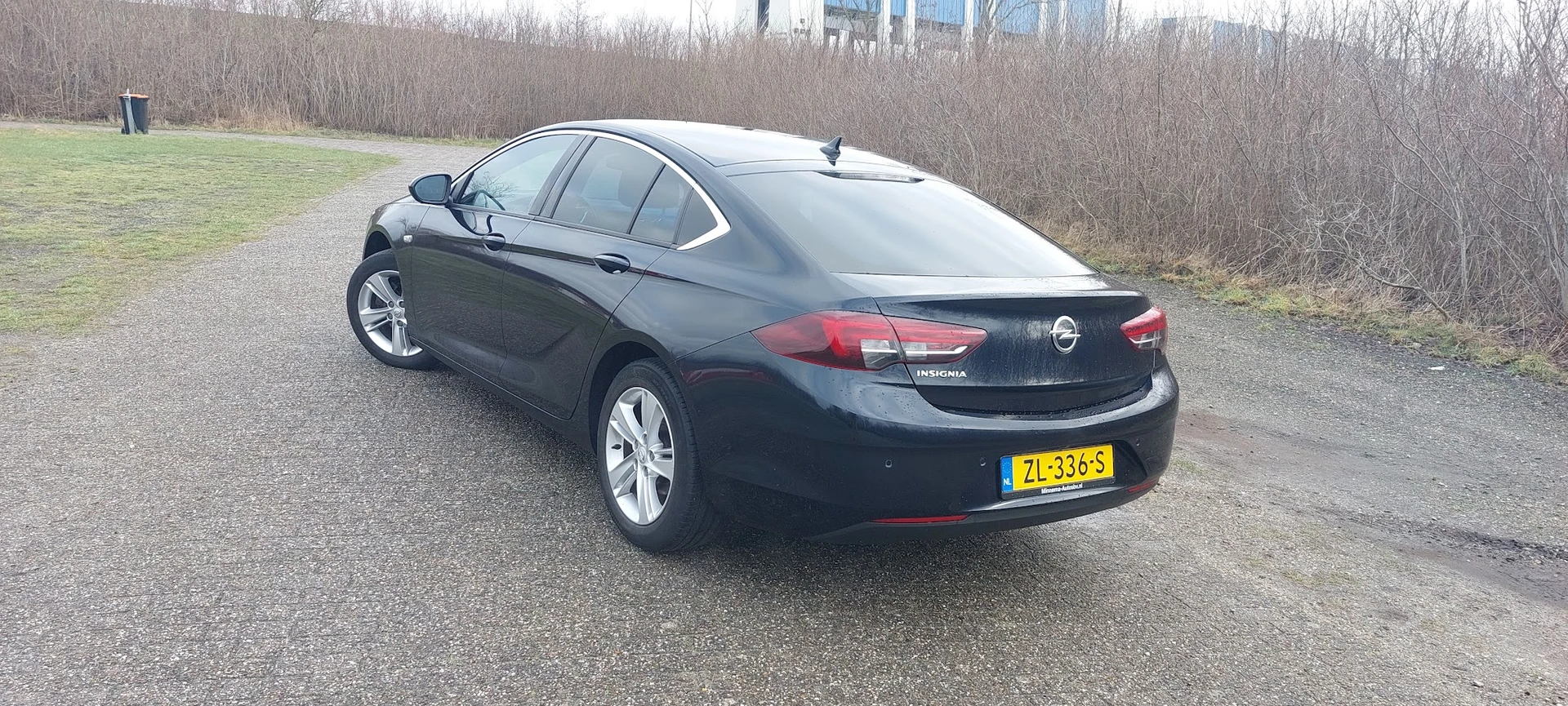 Zwarte Opel Insignia sedan op parkeerterrein, zijkant zichtbaar met kentekenplaat