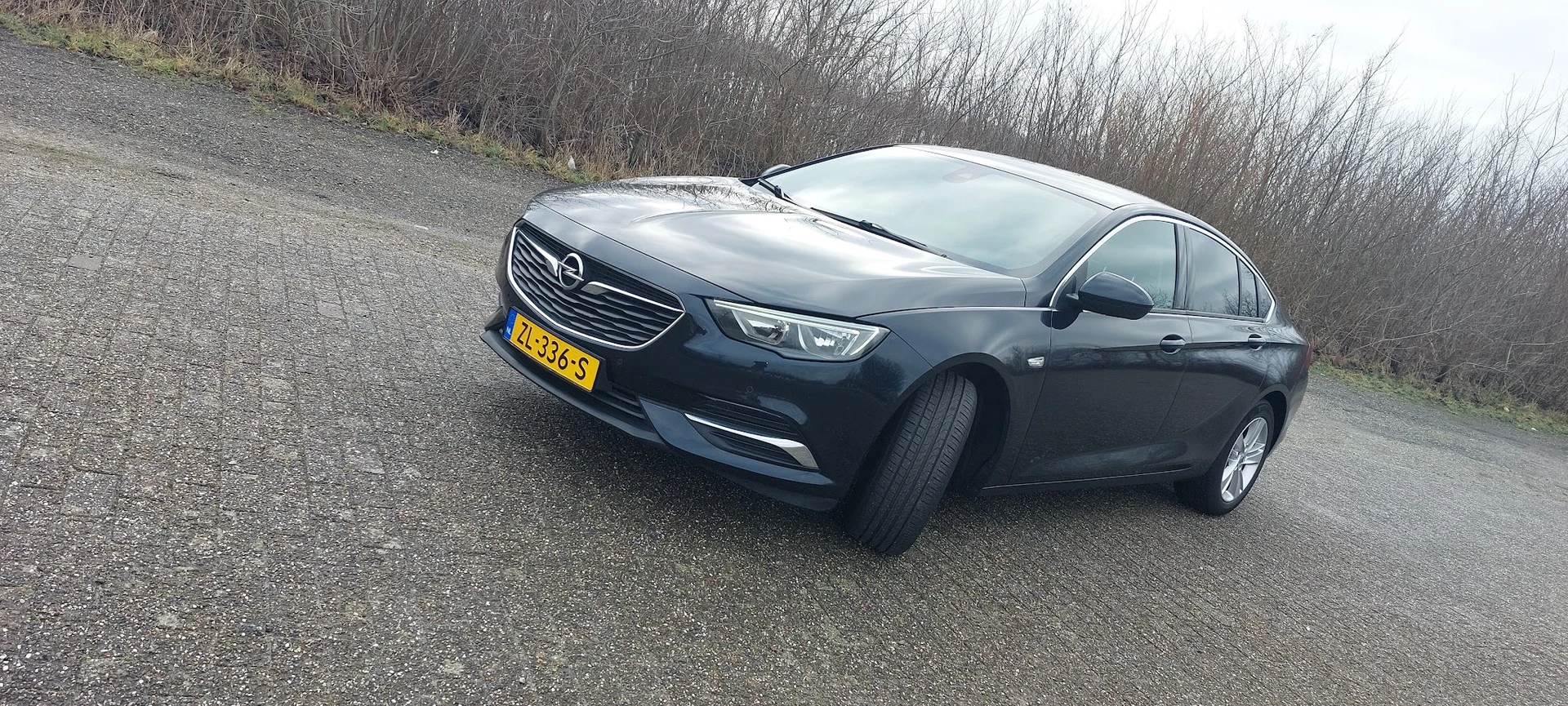 Donkerblauwe Opel Insignia sedan geparkeerd op grindpad