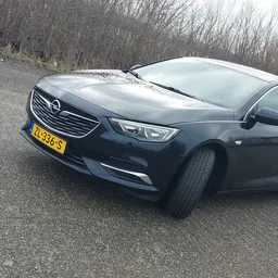 Donkerblauwe Opel Insignia sedan geparkeerd op grindpad