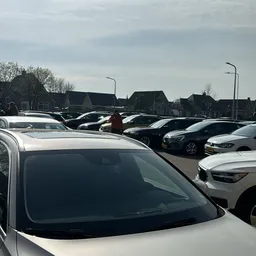 Parkeerplaats met meerdere tweedehands auto's te koop, huizen op achtergrond