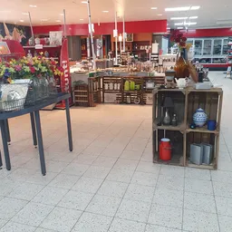 Winkelvloer met houten meubels, decoratieve items in stellingen en bloemstukken op tafel