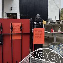 Voorkant van kringloopwinkel met rode deuren en openingstijden op bord