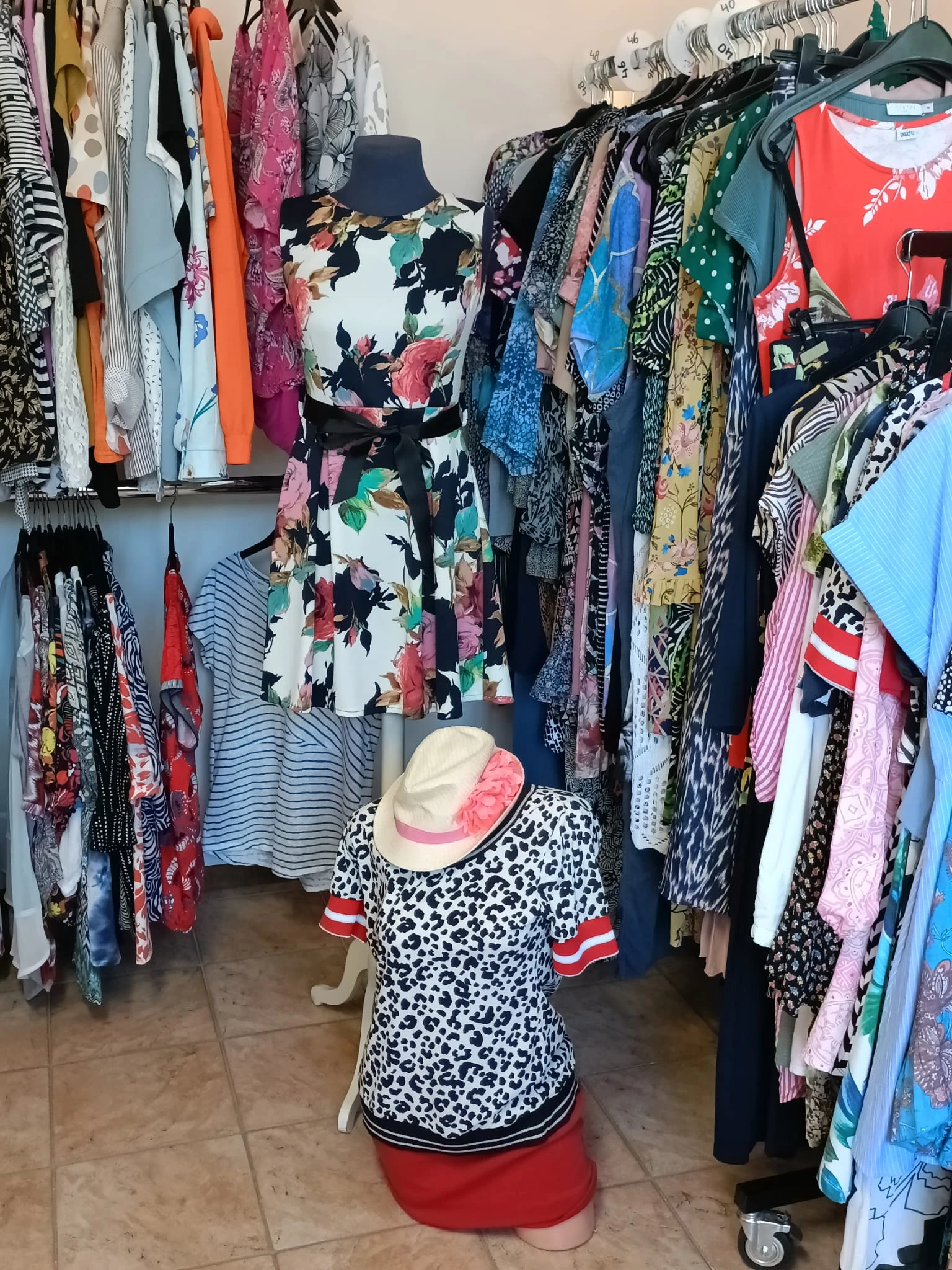 Rekken met tweedehands dameskleding in verschillende kleuren en patronen, met een shopster die een jurk bekijkt.