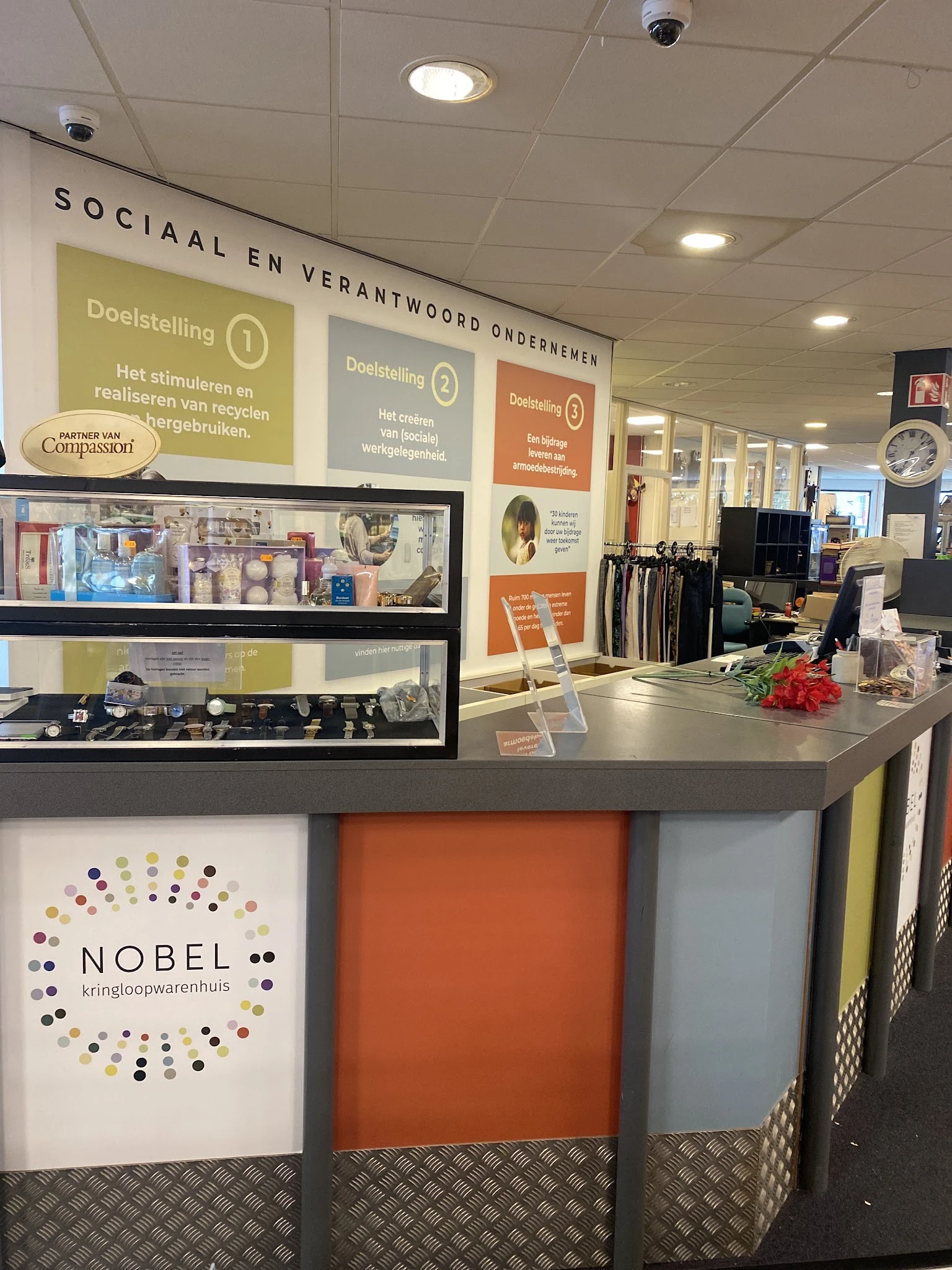 Winkelinterieur met toonbank, sieradenvitrines, wandpanelen met doelstellingen en kleding op hangers op de achtergrond