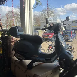 Zwarte scooter/Vespa met zwart zadel in uitstalling buiten voor de winkel