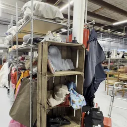 Houten stellingkast met gestapelde gestreepte borden en huishoudtextiel in een kringloopwinkel