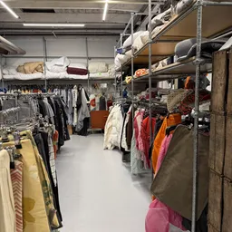 Winkelvloer met kledingrekken, stellingen met textiel en huishoudspullen
