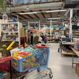 Winkelvloer met blauwe winkelkar vol kleding, stellingen met textiel en huishoudspullen in de achtergrond