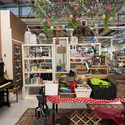 Winkelinterieur met witte stellingen vol spullen, hangende decoraties en een tafel met manden en kleding op de voorgrond