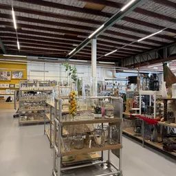Ruim winkelinterieur met glazen vitrinekasten vol huishoudartikelen, decoraties en kandelaars onder industriële plafondstruct