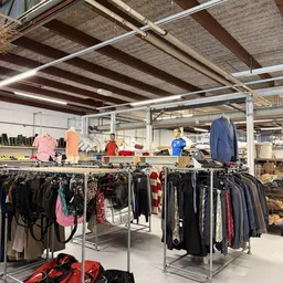 Rekken met tweedehands kleding, onder meer jassen en jurken, in een kringloopwinkel met betonnen plafond