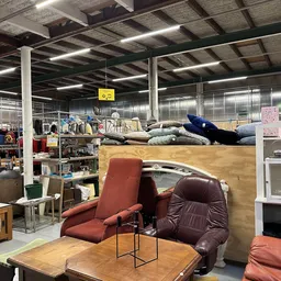 Tweedehands meubels en huishoudartikelen uitgestald in een kringloopwinkel, waaronder rode en bruine fauteuils op de voorgron