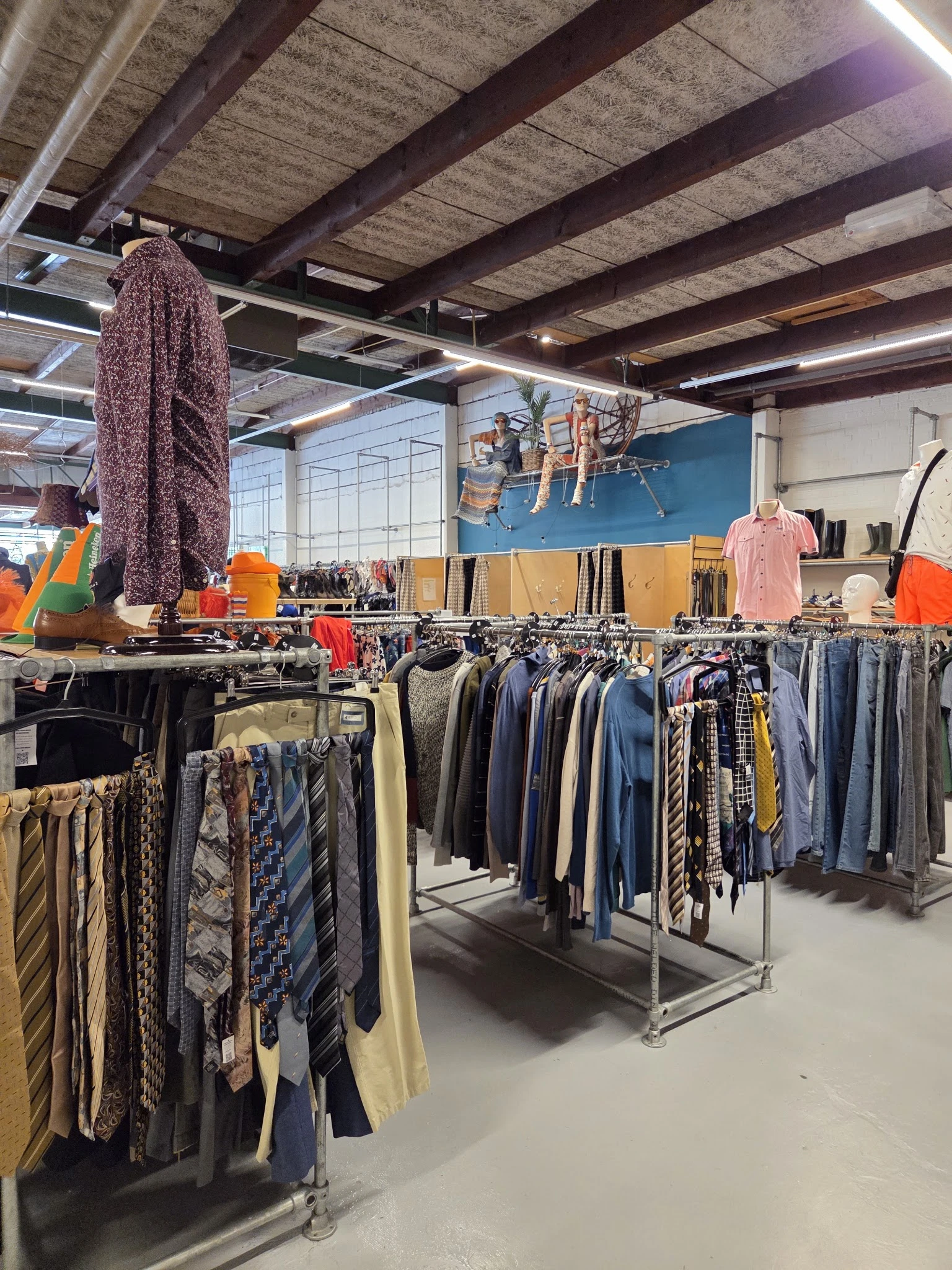 Rekken met tweedehands kleding, waaronder broeken, truien en andere kledingstukken in verschillende kleuren
