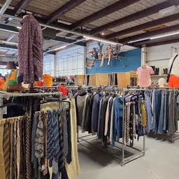 Rekken met tweedehands kleding, waaronder broeken, truien en andere kledingstukken in verschillende kleuren