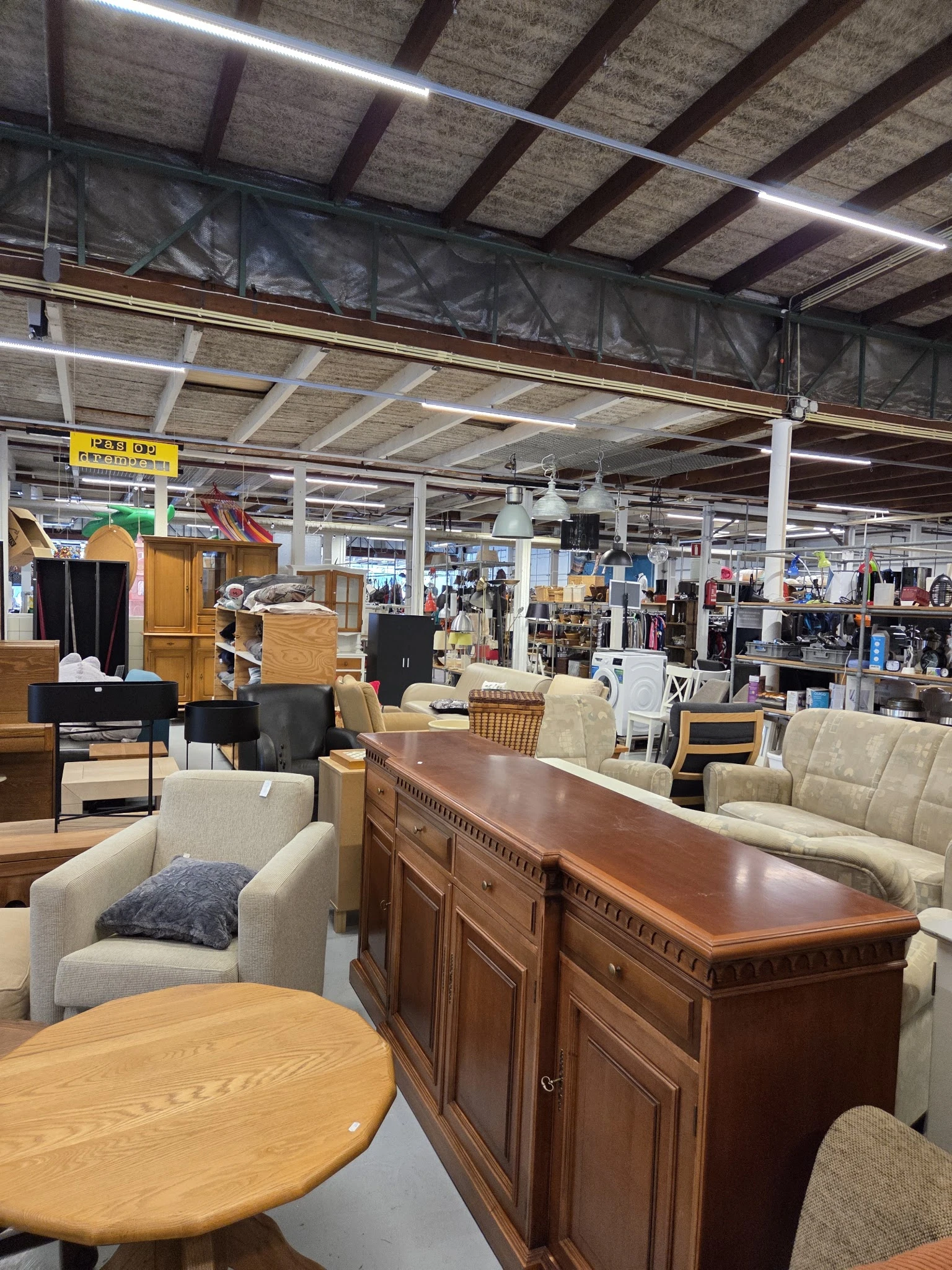 Winkelvloer met diverse meubels: fauteuils, kasten, tafels en andere huisraad uitgestald in een grote kringloopwinkel
