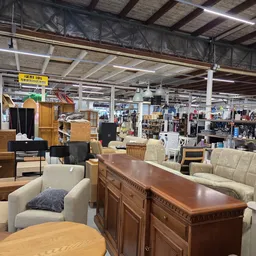 Winkelvloer met diverse meubels: fauteuils, kasten, tafels en andere huisraad uitgestald in een grote kringloopwinkel