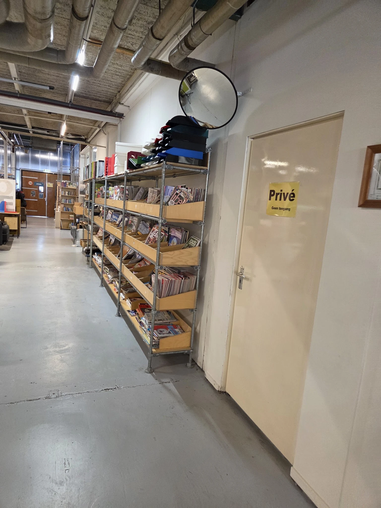 Winkelinterieur met metalen stellingen vol tweedehands spullen, deur met 'Privé' bordje zichtbaar