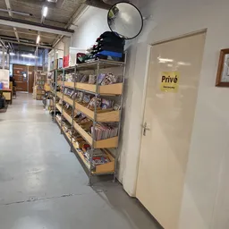Winkelinterieur met metalen stellingen vol tweedehands spullen, deur met 'Privé' bordje zichtbaar