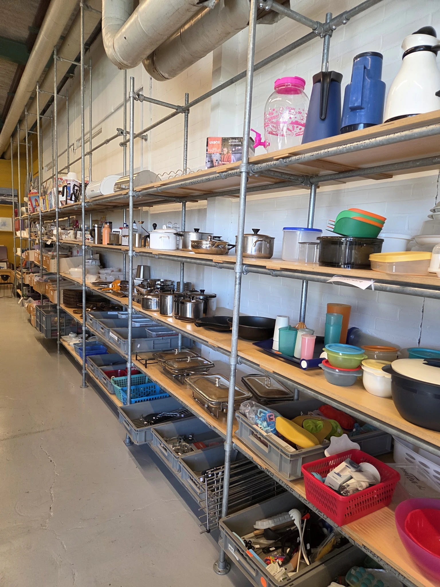 Metalen stellingen gevuld met diverse keukenartikelen, pannen, potjes en voedselcontainers