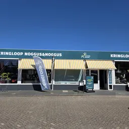 Voorgevel van kringloopwinkel met geel-wit gestreepte luifels, groene balk met winkelnaam en logo.