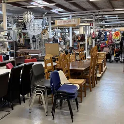 Winkelvloer met houten eettafels, stoelen in verschillende kleuren, en diverse artikelen op de achtergrond