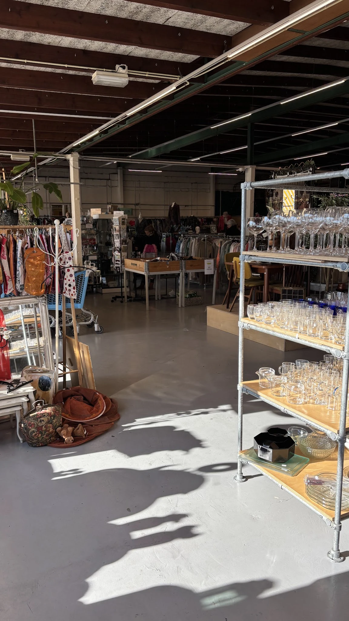 Winkelvloer met stellingen vol glazen, kleding aan rekken en diverse spullen uitgestald