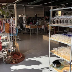 Winkelvloer met stellingen vol glazen, kleding aan rekken en diverse spullen uitgestald