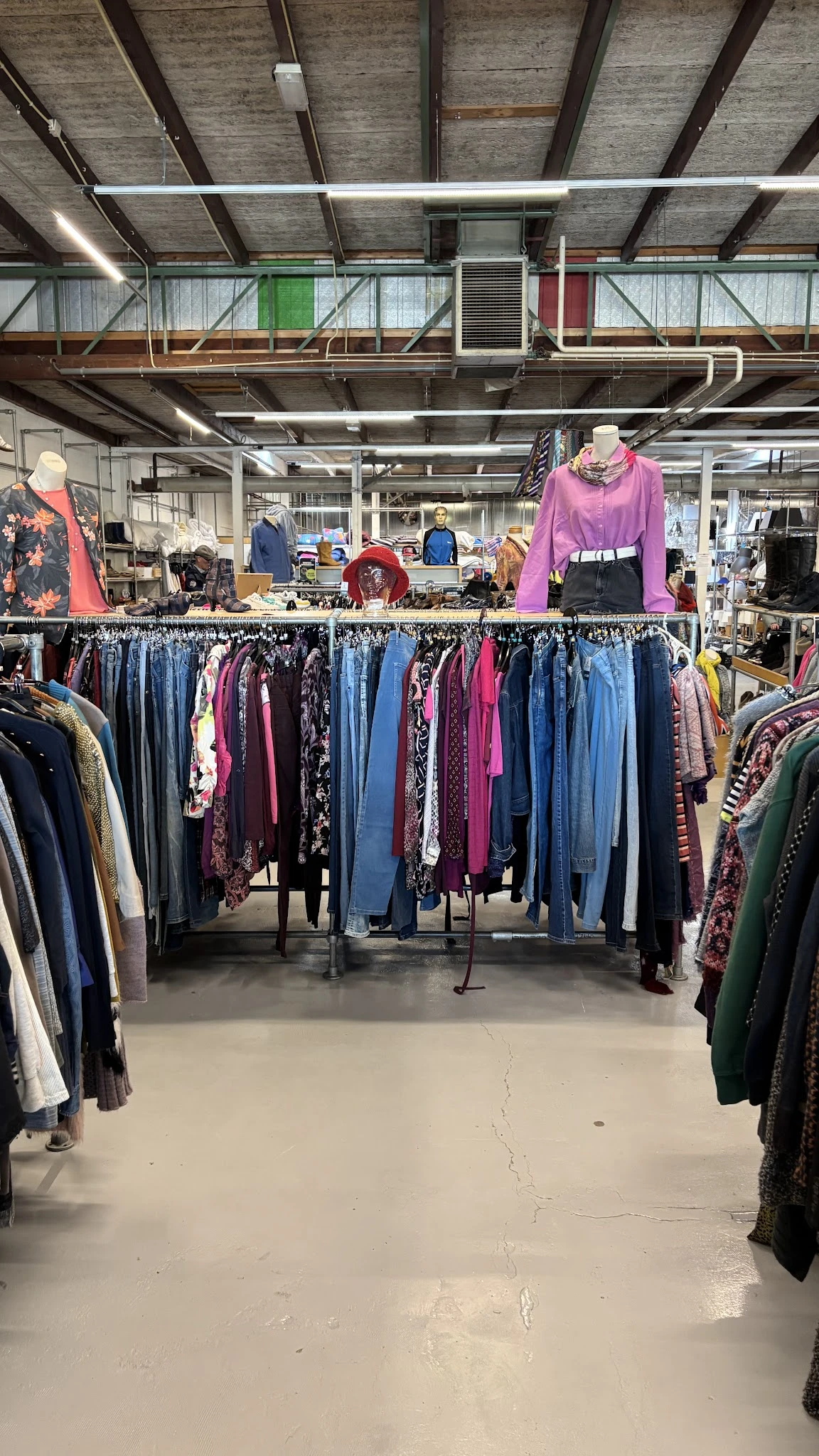 Rekken met tweedehands kleding in verschillende kleuren en stijlen, met displays van outfits boven de rekken