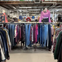 Rekken met tweedehands kleding in verschillende kleuren en stijlen, met displays van outfits boven de rekken