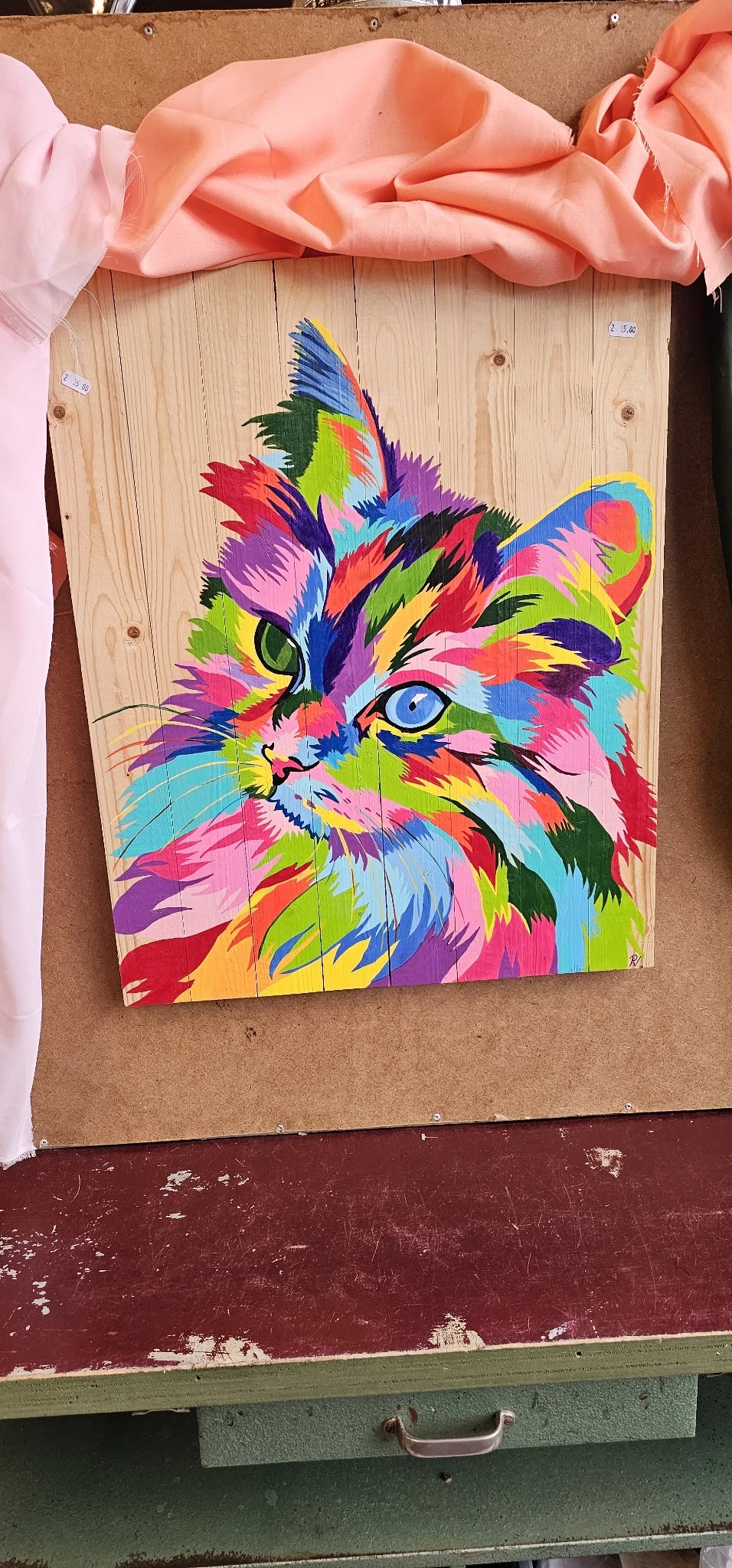 Kleurrijke pop-art schildering van een kat op hout, met fel gekleurde geometrische vlakken in roze, geel, blauw en groen